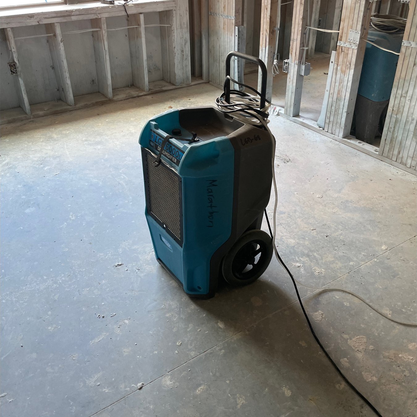 Commercial dehumidifier running in a stripped room with the lower drywall removed after water intrusion