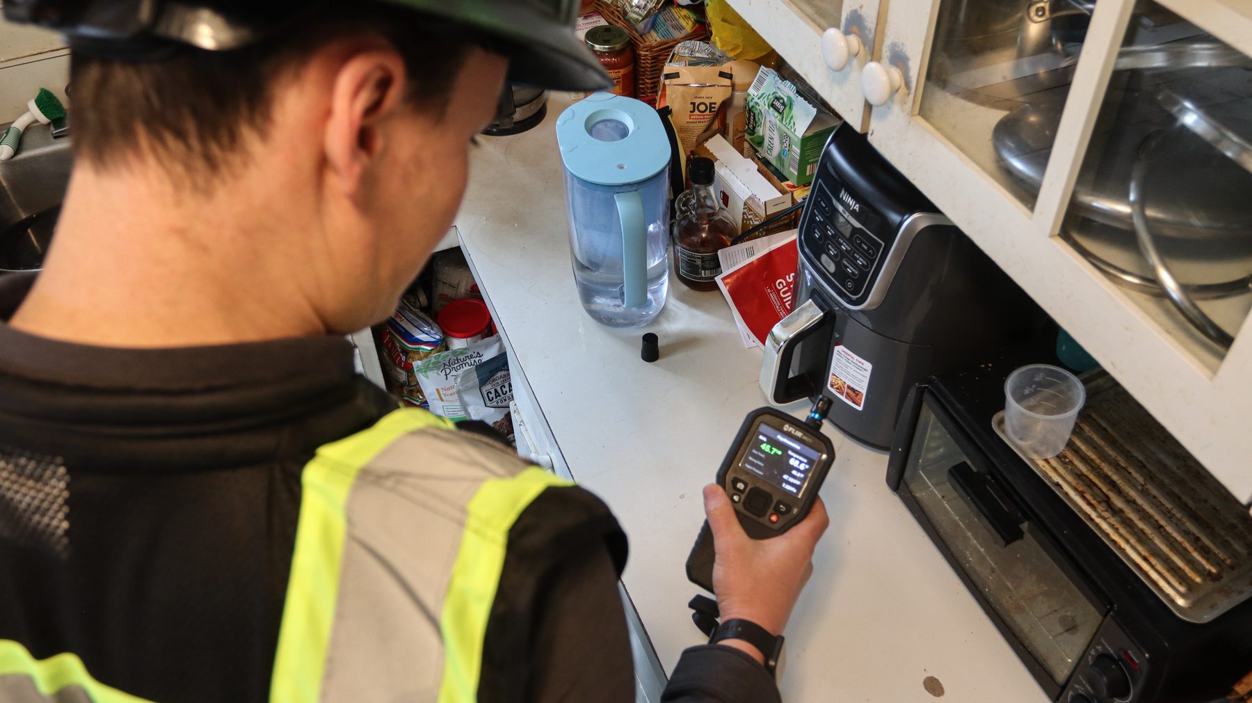 Prescient Environmental inspector taking a moisture reading on a kitchen wall with a pin moisture meter